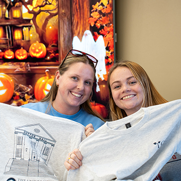 two female students hold up t shirts for the camera. guyton hall graphic shown on one