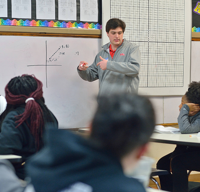 a male teacher explain graphing to students. a white board has a black graph on it